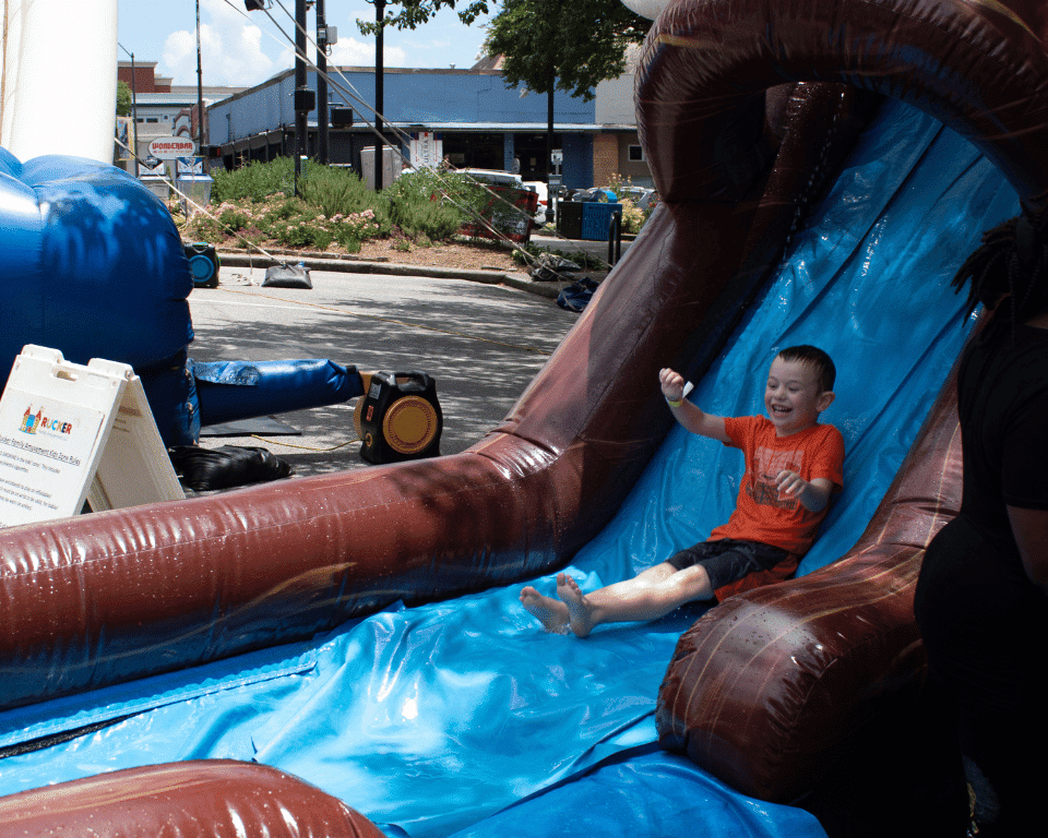 A kid slides down a waterslide at KidsFest at AthFest 2024.